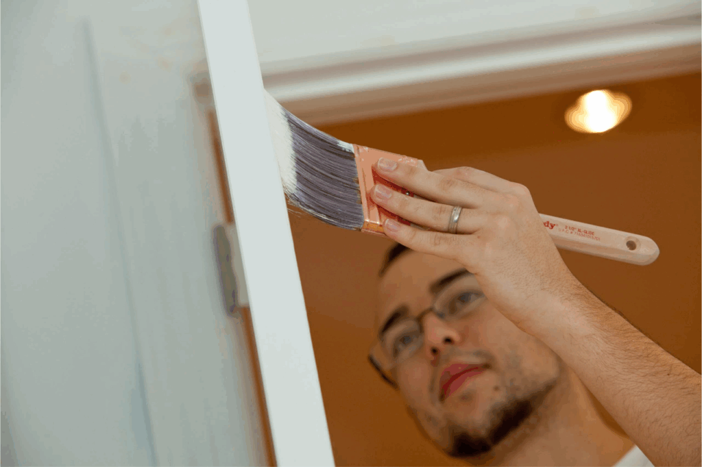 Close-up of a professional A.G. Williams painter carefully applying white paint to a door frame with a precision brush, showcasing painting contractor tips in action.