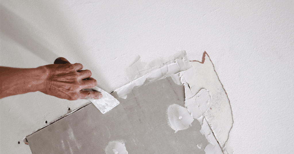Hand applying joint compound to repair damaged drywall after ice dam and burst pipe water intrusion.