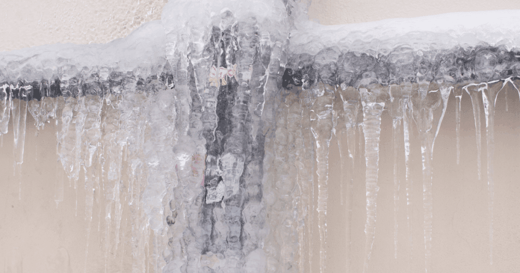 Frozen outdoor spigot with ice buildup against painted exterior siding, highlighting winter weather risks to home exteriors.
