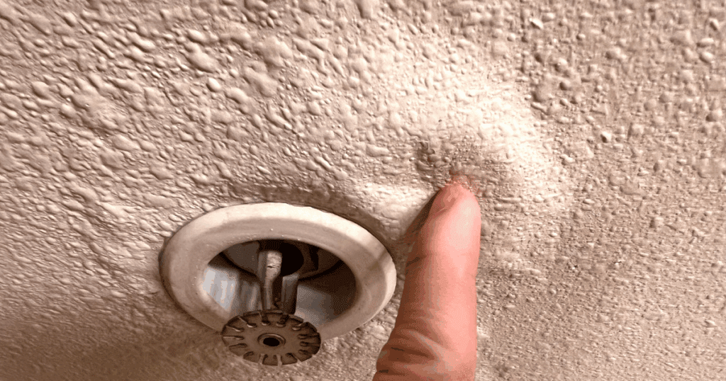 Textured ceiling with water staining and moisture buildup around a recessed fire sprinkler head.