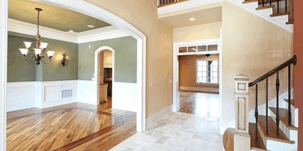 Open foyer and dining space with sage green and beige walls, white wainscoting, and hardwood flooring.
