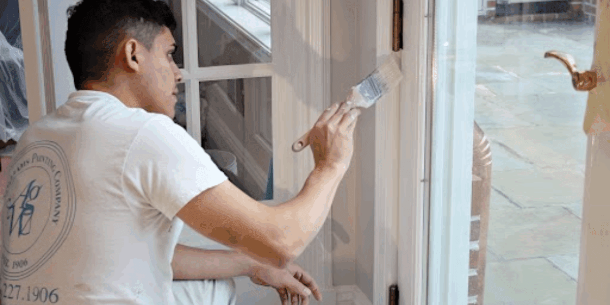 Close-up of a professional A.G. Williams painter carefully applying white paint to a door frame with a precision brush, showcasing painting contractor tips in action. Avoid these common house painting mistakes with tips from A.G. Williams.